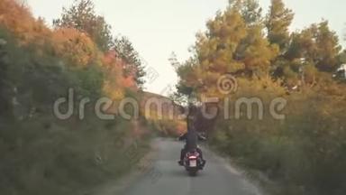 从后面的人骑摩托车在森林道路上。 库存。 黑色皮夹克摩托车手的美丽景色